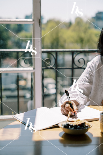 Woman writing in a notebook while eating breakfast in a calm, cozy space. Wellness stock images for lifestyle bloggers, coaches, and intentional living content.