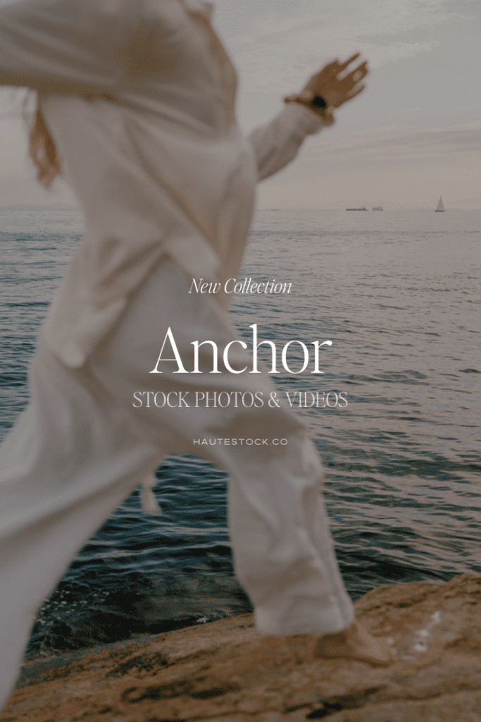 Woman in flowing neutral clothing standing by the ocean with arms open, representing calm, renewal, and grounded coastal brand imagery.